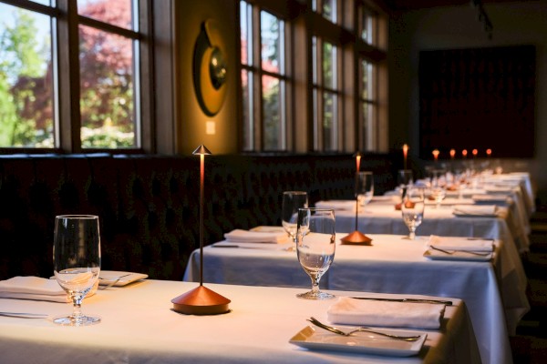 A dimly lit restaurant with white tablecloths, glassware, and small lamps, creating an elegant and intimate dining atmosphere.