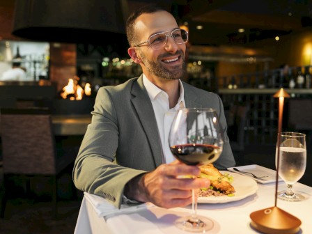 A man in a grey suit enjoys a glass of red wine and a delicious meal at a cozy, elegant restaurant.