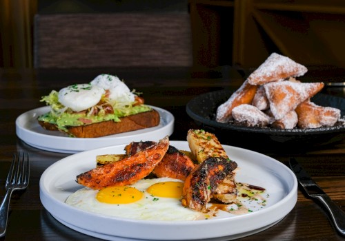 A breakfast plate with eggs, grilled chicken, and roasted vegetables, a toast with avocado and poached eggs, and a bowl of fried pastry dusted with powdered sugar.