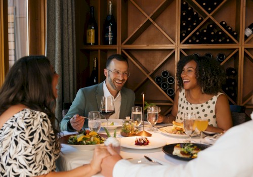 A diverse group of people enjoying a joyful dinner with wine, salad, and desserts in a warmly lit, elegant restaurant setting.