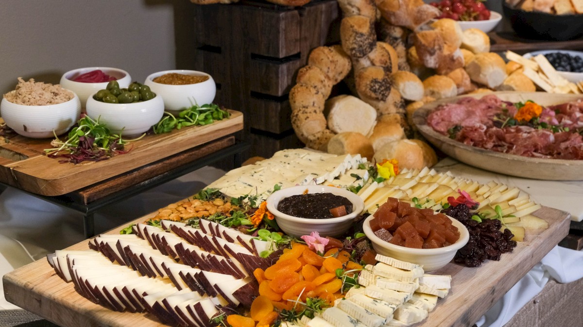 A cheese and charcuterie spread with breads, dips, fruits, and various accompaniments on wooden platters.