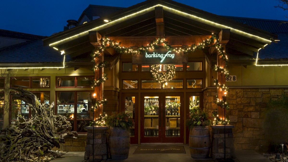 A warmly lit restaurant entrance with festive lights and rustic decor, displaying the name 