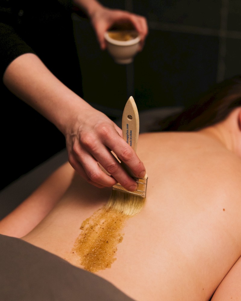 A person receives a hot stone massage, with massage oil being applied to their back during the treatment.
