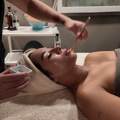 A woman is getting a facial treatment with a brush applied to her face in a spa setting.