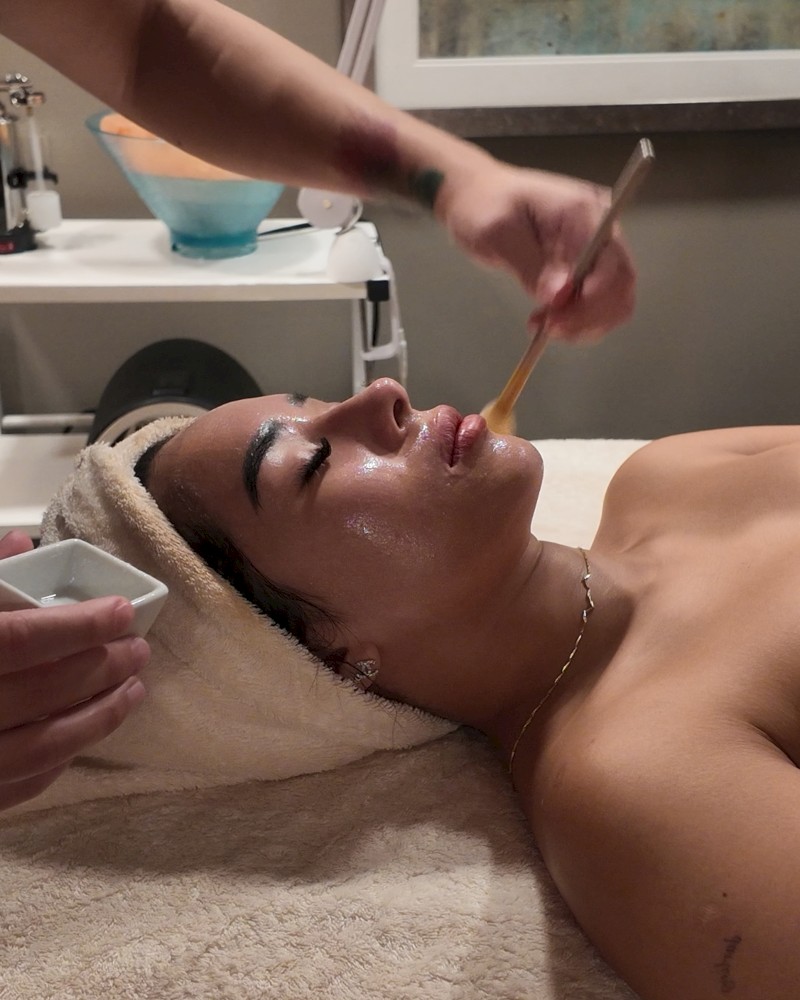 A woman is getting a facial treatment with a brush applied to her face in a spa setting.
