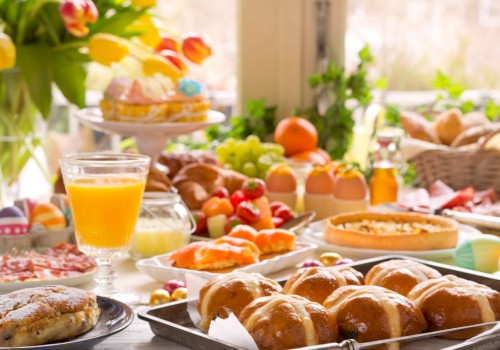 A colorful breakfast spread features pastries, fruits, eggs, juice, and baked goods on a sunny table.