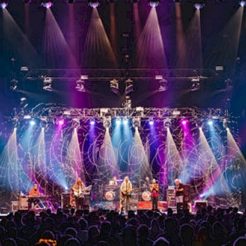 A live concert with a band performing on stage under colorful lighting, audience enjoying the show in a darkened venue.