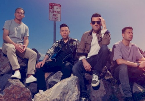 Four men sit on rocks by the water under a 