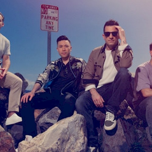 Four men sit on rocks by the water under a 