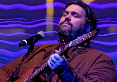 A man is serenading with a guitar and singing passionately against a vibrant, colorful, wavy background.