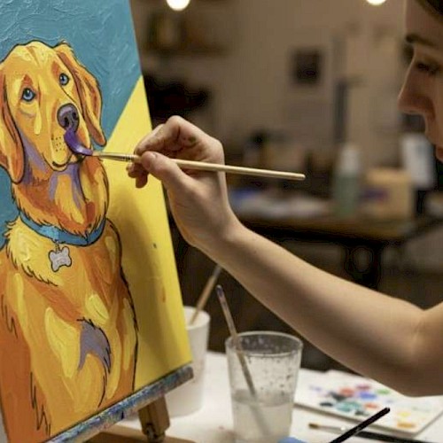 A person paints a colorful, cartoon-style portrait of a golden retriever dog on a canvas in an art studio.