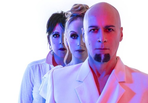 Three people stand closely against a white background, with dramatic blue and red lighting highlighting their faces and clothing.