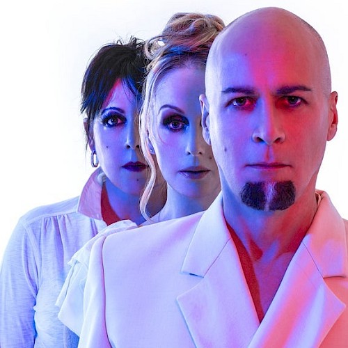 Three people stand closely against a white background, with dramatic blue and red lighting highlighting their faces and clothing.