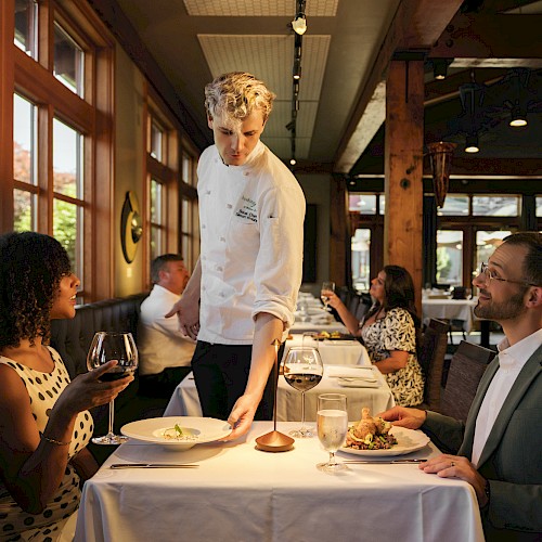 A waiter serves food to a woman and man at a restaurant table during a pleasant dining experience.
