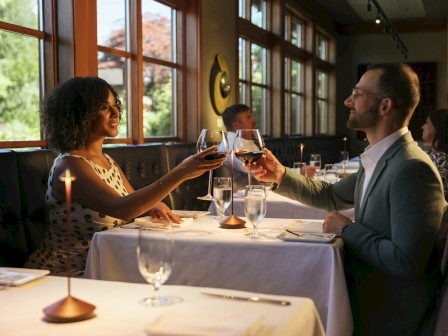A couple toasting with glasses of red wine at a cozy restaurant during a special occasion.