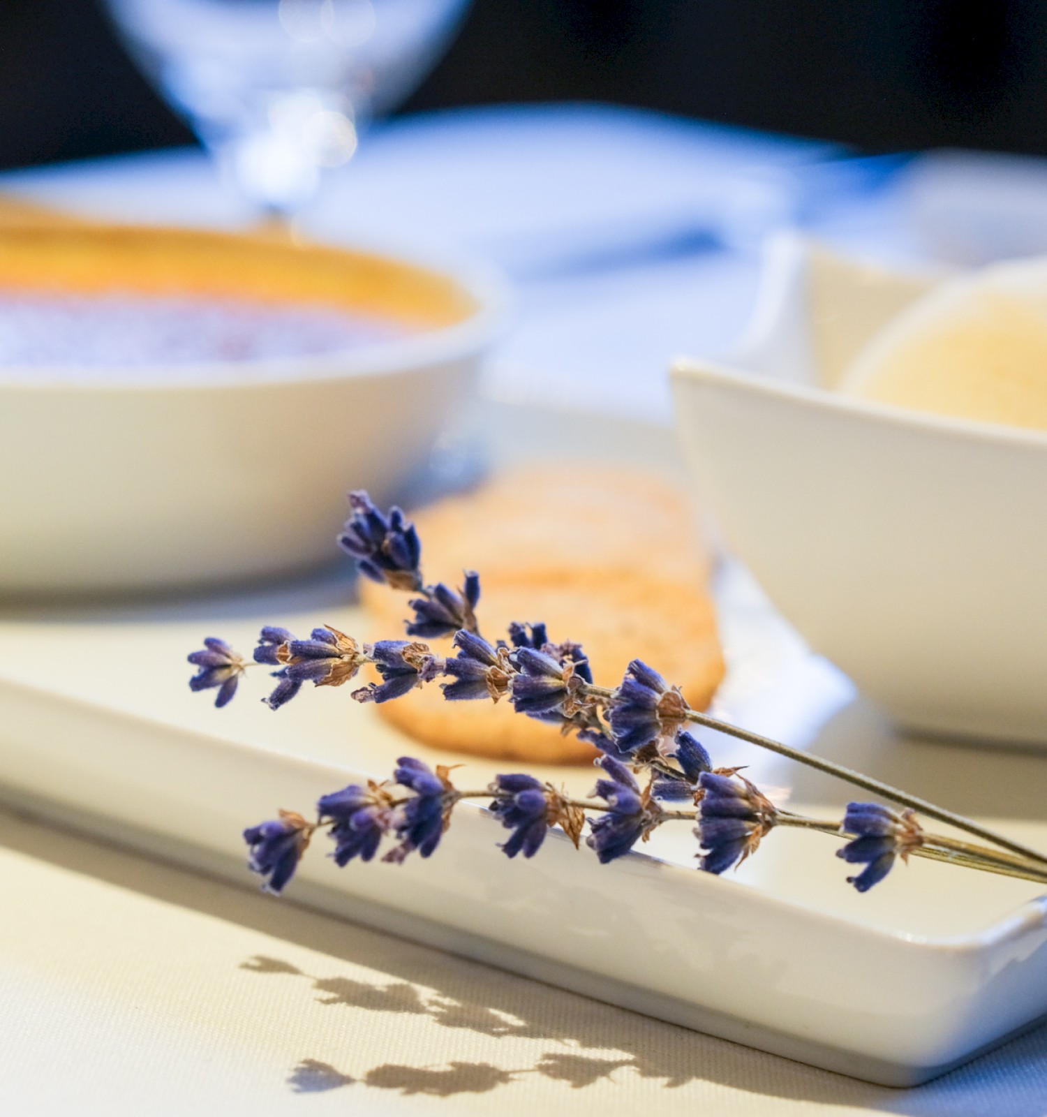 A table setting with bowls of ice cream, a sprig of lavender, and a white plate, creating a calm and elegant dessert presentation.