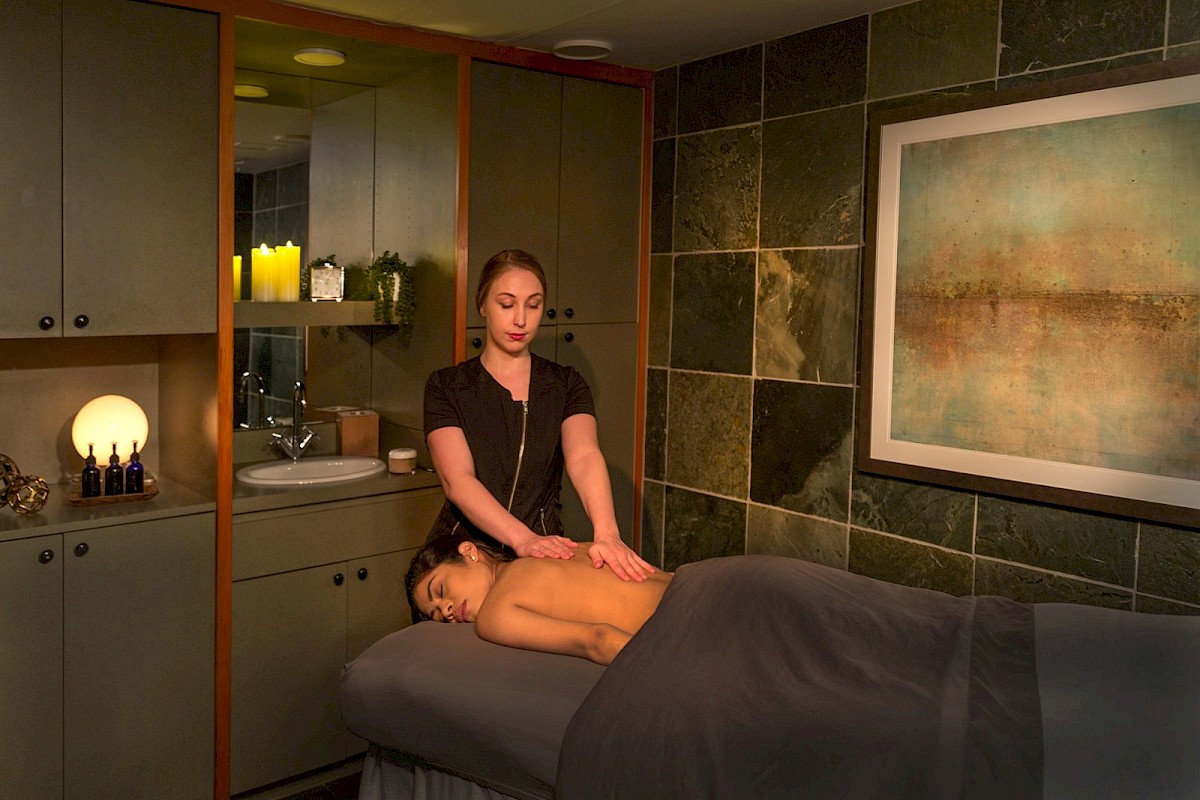 A woman is giving a massage to a woman lying face down on a massage table in a cozy, dimly lit room.