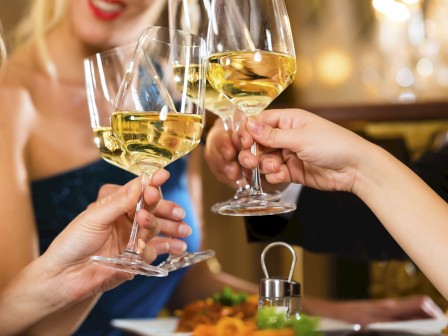 People clinking glasses of white wine in a celebratory toast at a dinner.