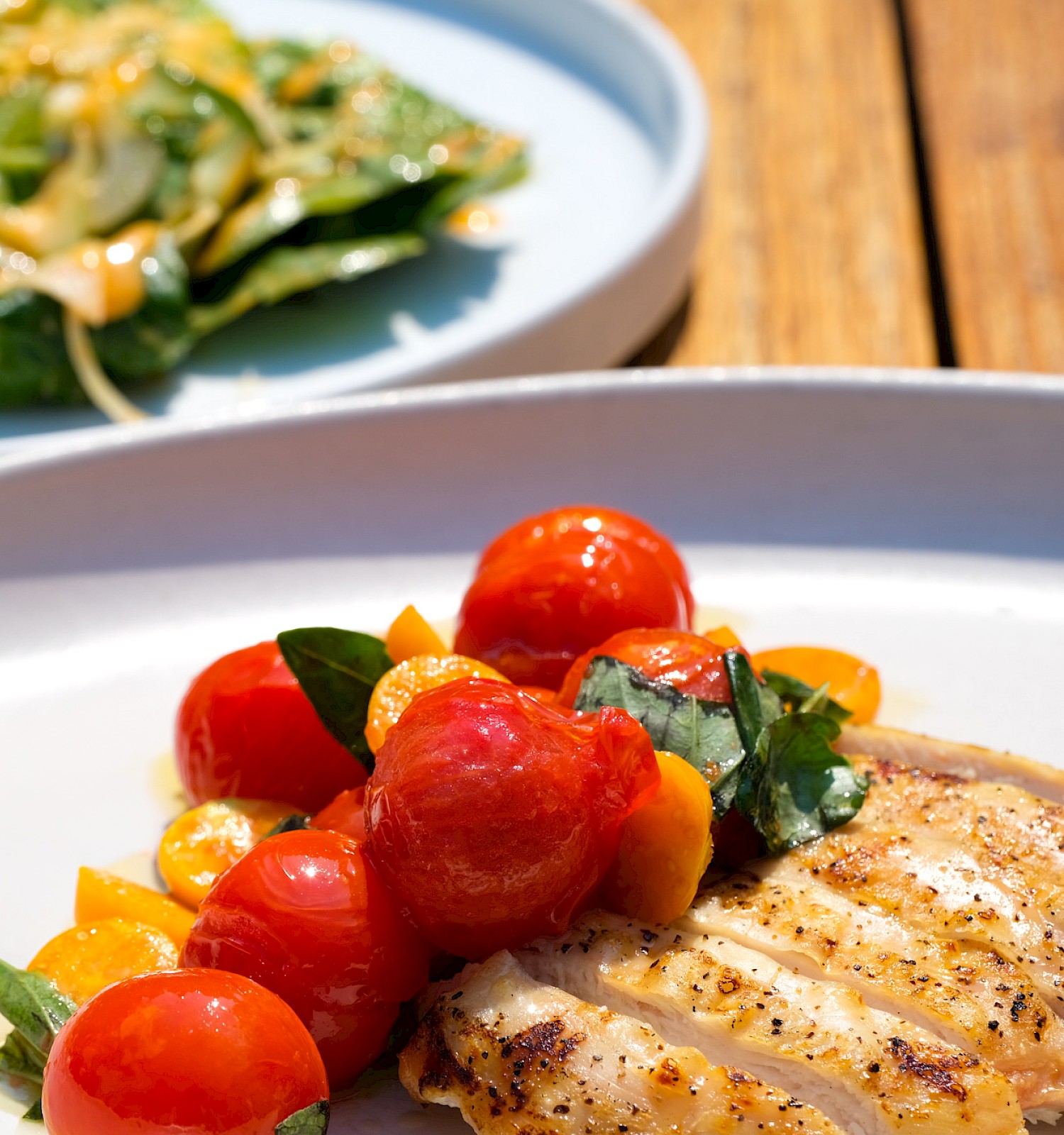 The image shows a plate with cooked chicken, cherry tomatoes, and basil, alongside a salad with greens and dressing on a white dish.