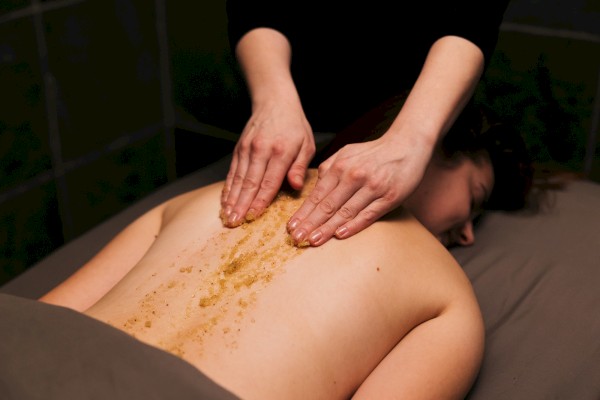 A person receives a back massage or treatment with a granular substance applied to their back in a spa or wellness setting.