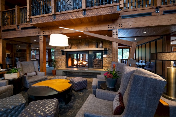 A cozy, rustic lounge with a stone fireplace, plush seating, wooden accents, and warm lighting creating inviting comfort.