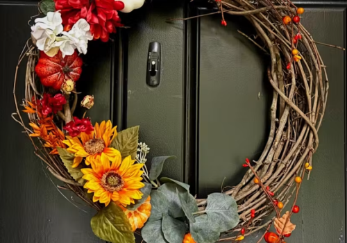 This is a decorative autumn wreath made of twigs, adorned with sunflowers, pumpkins, berries, and colorful flowers on a black door.