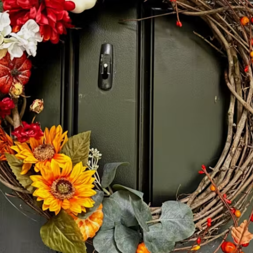 This is a decorative autumn wreath made of twigs, adorned with sunflowers, pumpkins, berries, and colorful flowers on a black door.