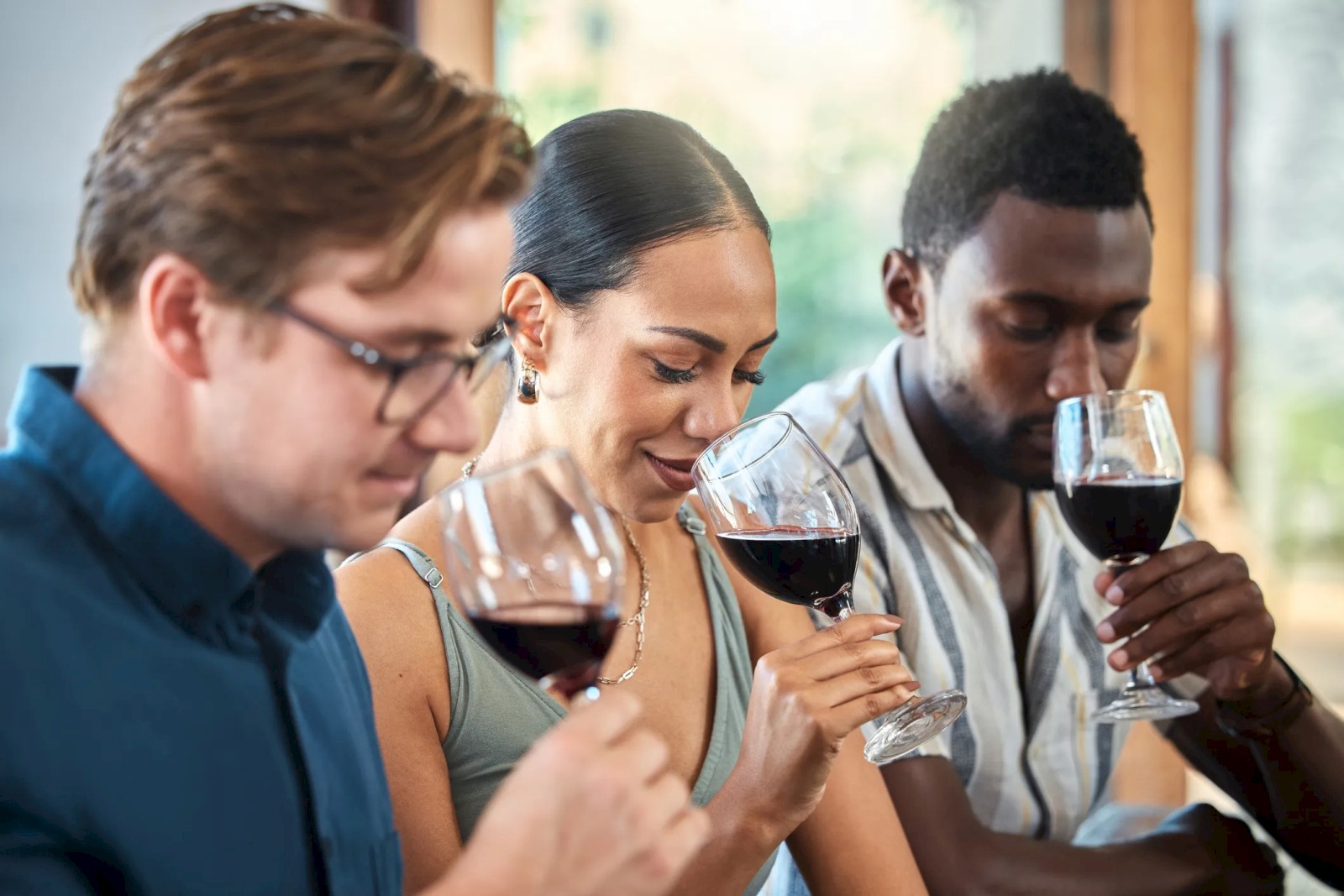 Three people are sitting and savoring wine, each holding a glass close to their nose, likely participating in a wine tasting event.