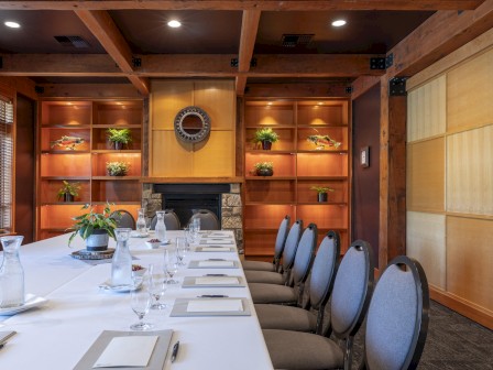 A formal dining room with a long table, set with glasses, napkins, and notepads, surrounded by chairs, and a decorated wooden interior.