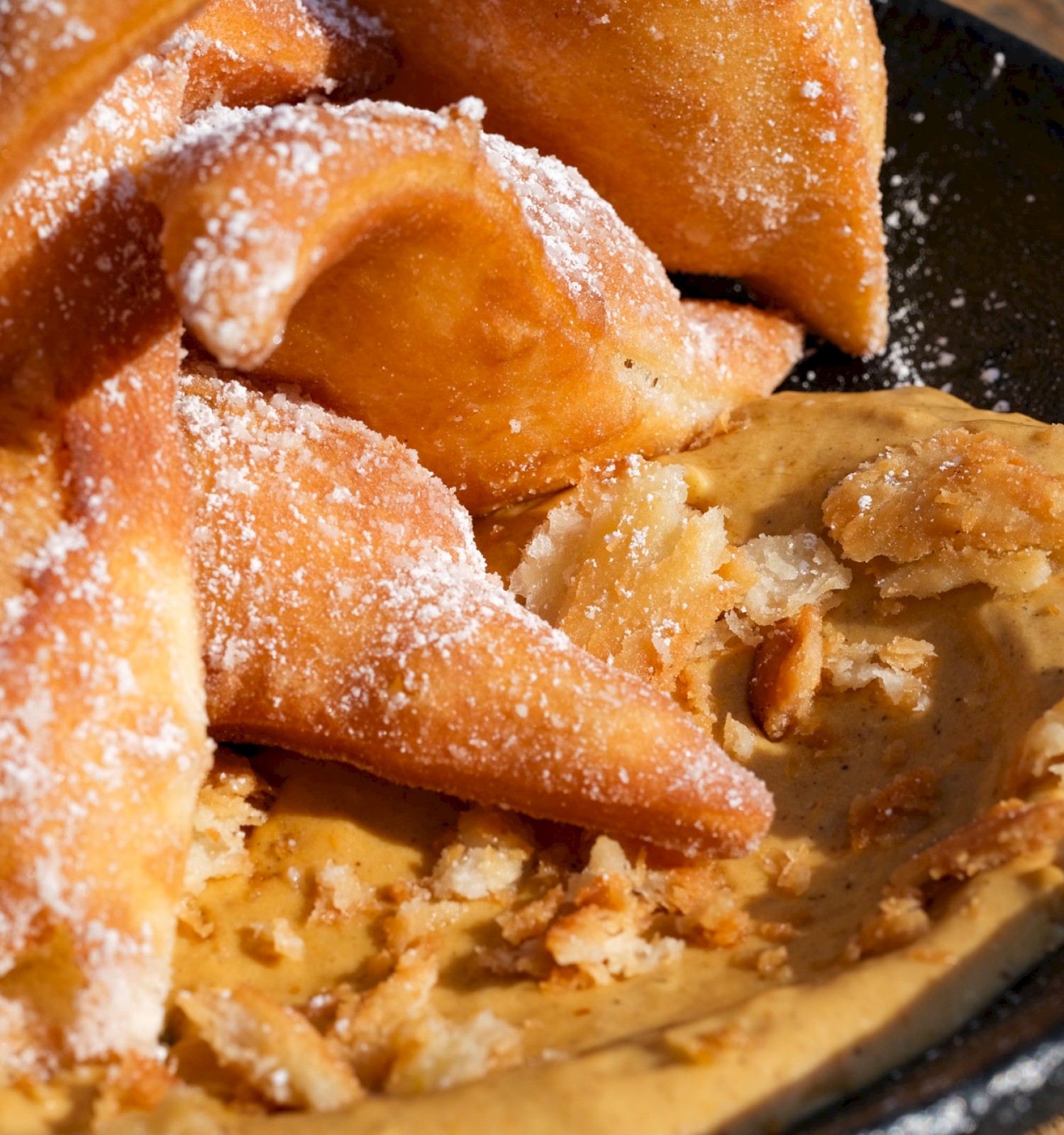 Fried plantains with peanut butter and a sweet, crumbly topping served in a black bowl on a wooden surface.