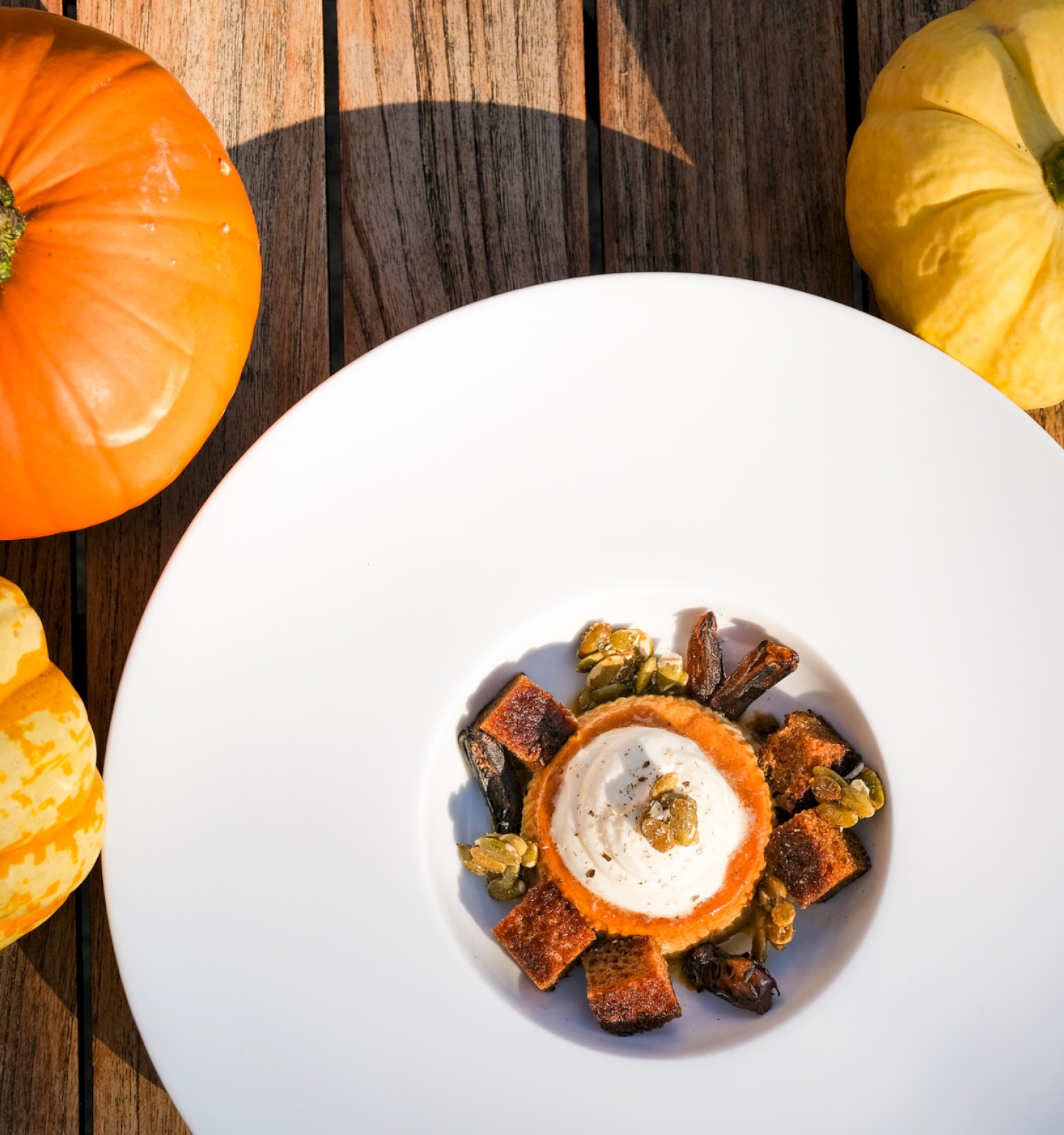 A plate of gourmet food with pumpkin, spices, and garnishes, surrounded by colorful heirloom pumpkins on a wooden surface.