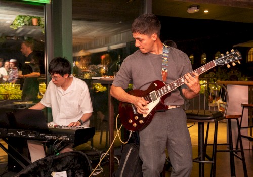 Musicians perform live jazz music at an indoor event, with one playing the keyboard and the other on an electric guitar.