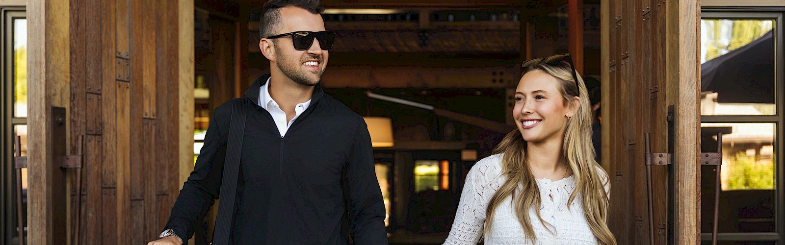 A couple is happily exiting a building with luggage, holding hands, and smiling, suggesting they might be on a trip or vacation.