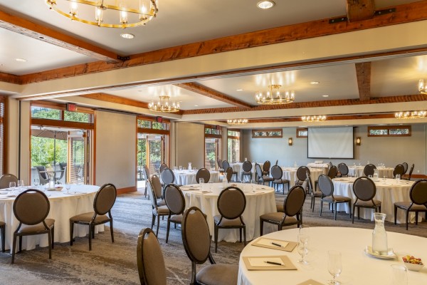 A spacious, well-lit conference room with round tables, chairs, and a projection screen, ready for a meeting or event.