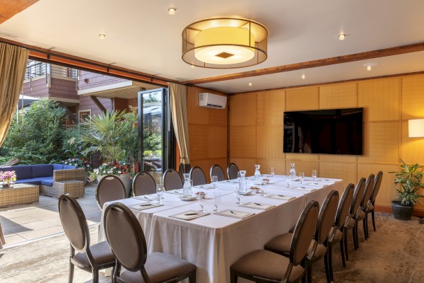 A formal dining room set for a meeting or event, with a view of an outdoor patio full of plants and seating areas.