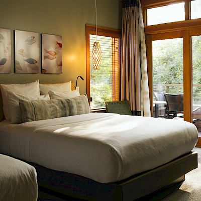 A cozy bedroom with a large bed, artwork, wooden window blinds, and a balcony with outdoor furniture.