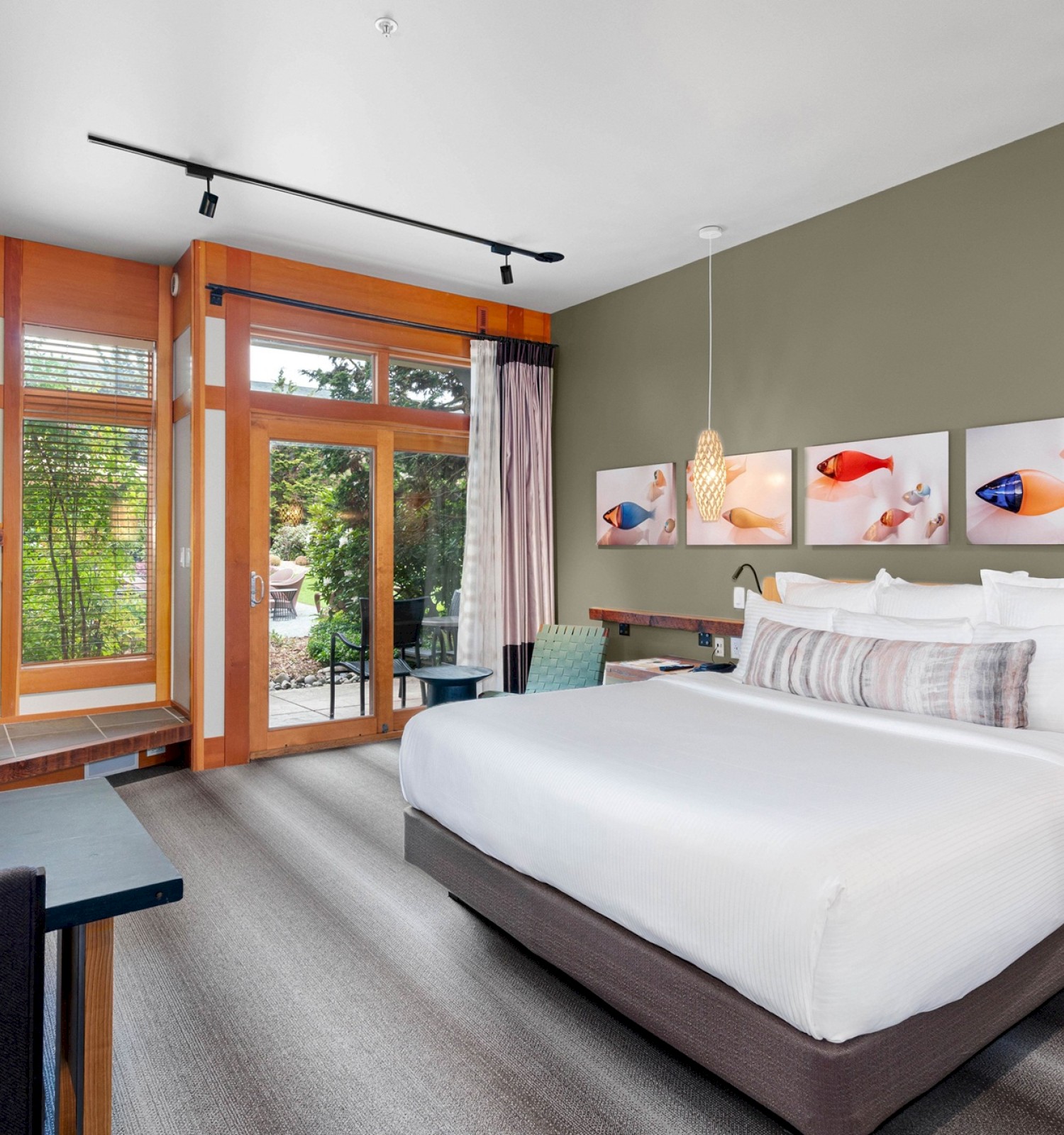 A cozy hotel room with a king-sized bed, a fireplace, artwork of fish on the wall, and a sliding glass door leading to a garden patio.