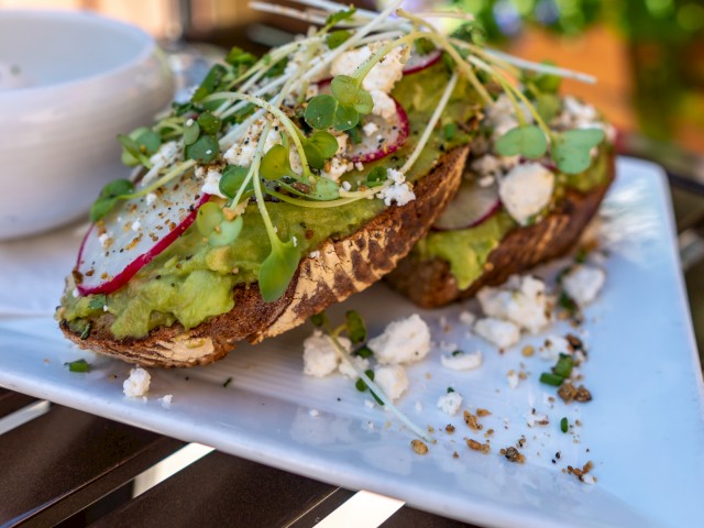 Open-faced toast topped with avocado, radishes, microgreens, feta, and seasonings on a white plate.
