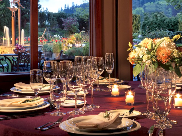 A beautifully set dining table with wine glasses, candles, and a flower arrangement overlooking a lush garden.