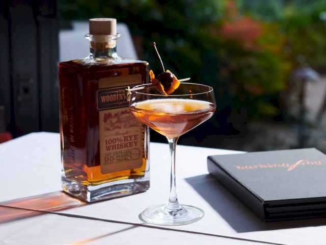 A whiskey bottle, a cocktail glass with garnishes, and a menu labeled 'bartering for' on a white tablecloth.