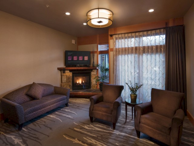Cozy living room with a fireplace, sofa, two armchairs, TV, and large window with sheer curtains letting in natural light.