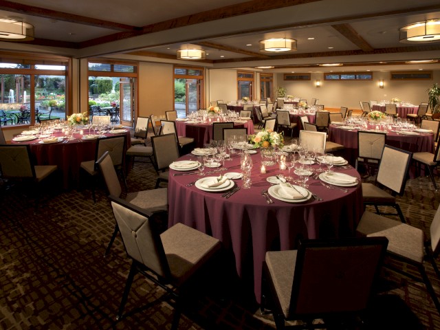 A beautifully set banquet room with round tables, elegant floral centerpieces, and a view of a garden outside.