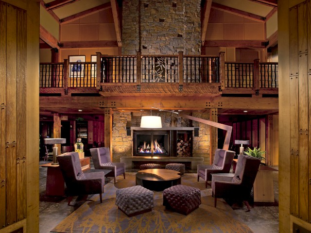 A cozy living room with a stone fireplace, purple chairs, wooden décor, and a mezzanine overlooking the space.
