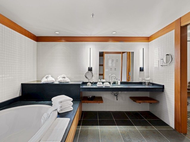 A modern, spacious bathroom with a bathtub, ample towels, a large mirror, and a walk-in shower area, all featuring a sleek and minimalist design.
