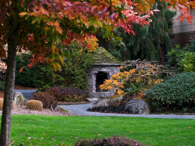 A peaceful garden scene with colorful autumn leaves, a small stone structure, and lush greenery.