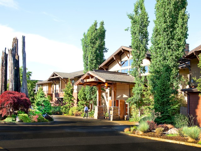 This image shows a peaceful residential apartment complex surrounded by lush green trees and landscaped gardens on a sunny day.