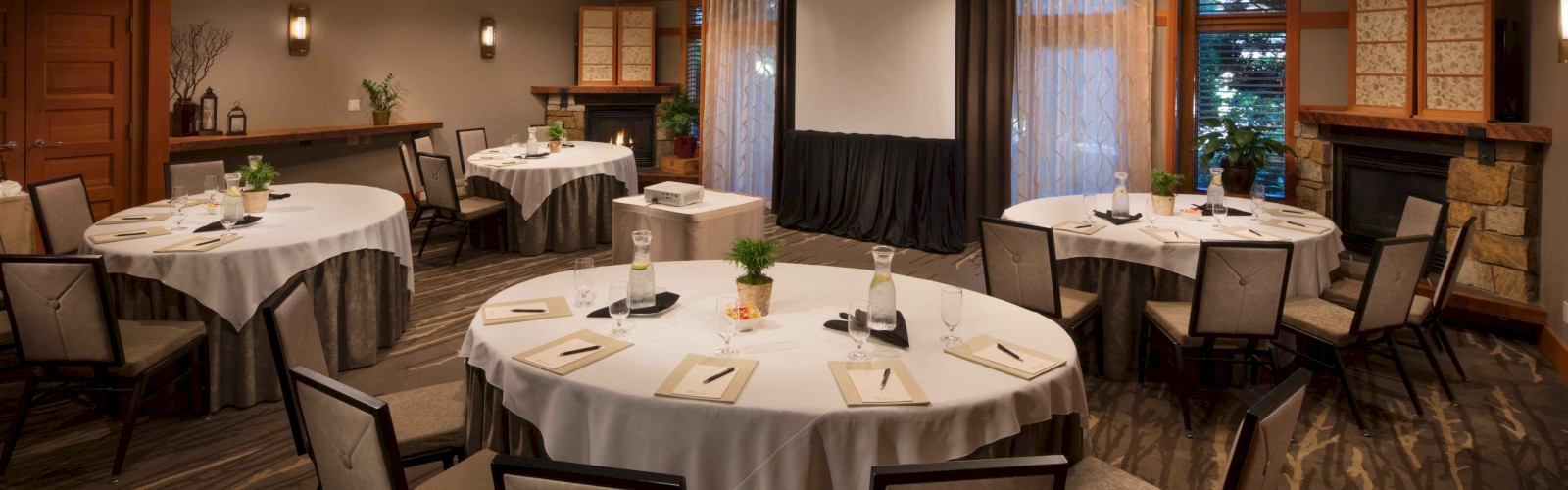 The image shows a conference room with round tables, chairs, a projector screen, and a cozy atmosphere.