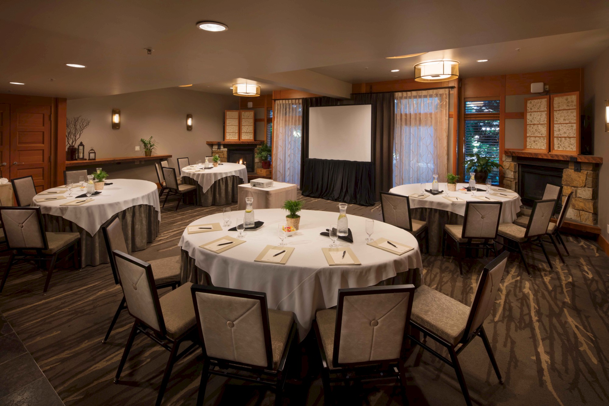 The image shows a conference room with round tables, chairs, a projector screen, and a cozy atmosphere.