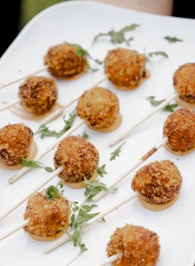 The image shows a platter of round, crispy appetizers on skewers, garnished with small green herbs, likely served as finger food.