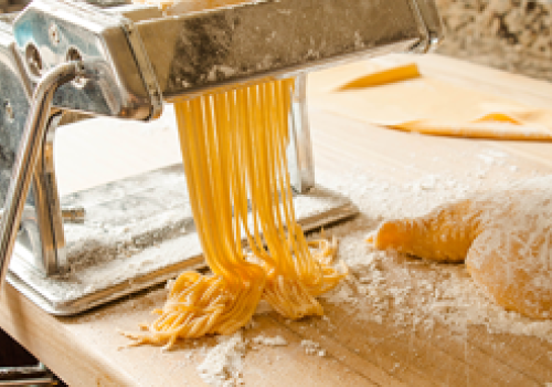 Fresh pasta being made with a pasta machine on a wooden surface, dusted with flour.